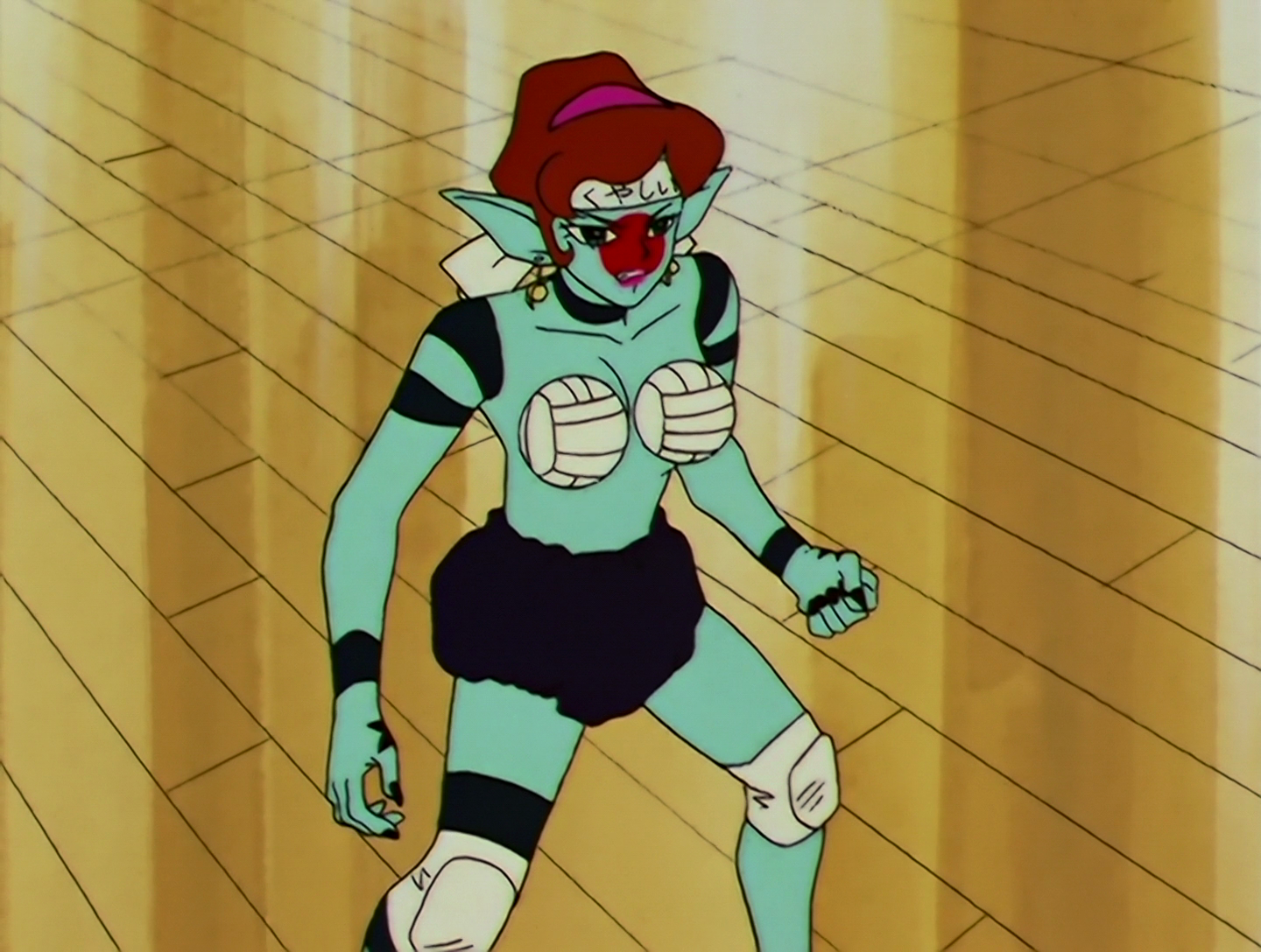 Haikyun, a Daimon from Sailor Moon episode 100. She has light turquoise skin with a large red circle on her face, and brown hair that’s tied back. She wears puffy black bloomers and her chest is covered by two half-volleyballs. She wears a headband that reads “kuyashii,” meaning “frustrated,” but the text on this changes frequently.